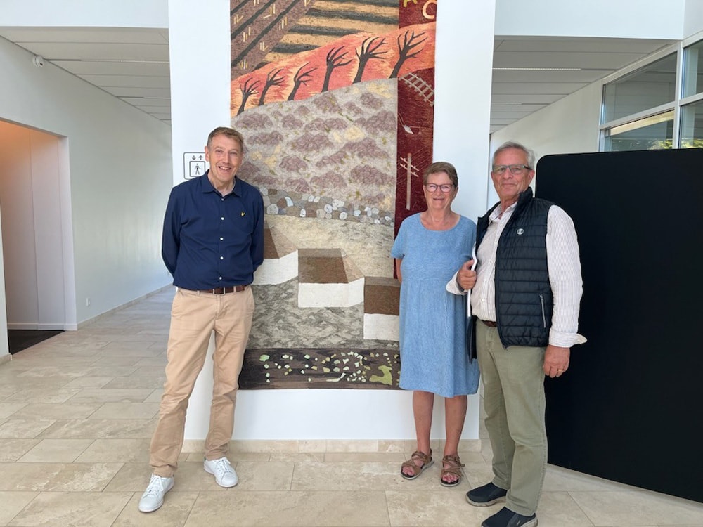 Jeremy Watts fra historiegruppen under Vorbasse Lokalråd, afdelingsdirektør H. C. Christensen fra Sparekassen Kronjylland og Inger Donslund fra frivilliggruppen under Vorbasse Bibliotek fotograferet foran vægtæppet i Sparekassen Kronjylland i Vorbasse.
