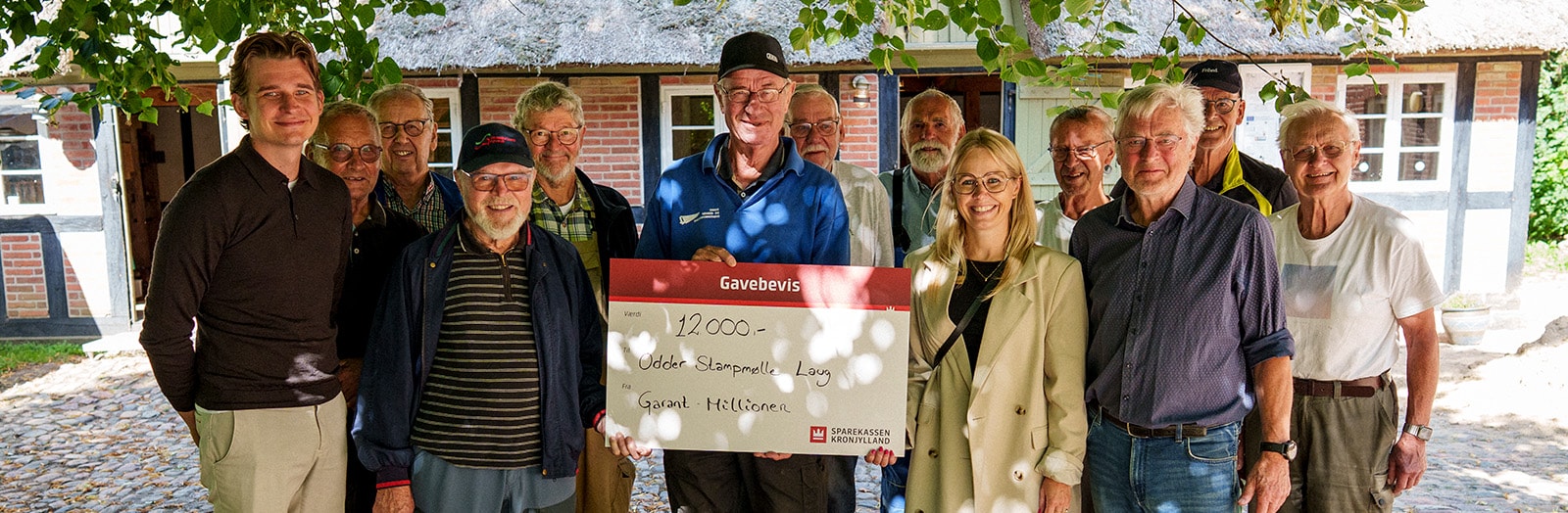 Afdelingsdirektør Mia Ann Rosendahl Kristensen og kunderådgiver Jens Meldgaard fra Sparekassen Kronjylland i Odder overrækker donationen til medlemmerne af Odder Stampmølle Laug.